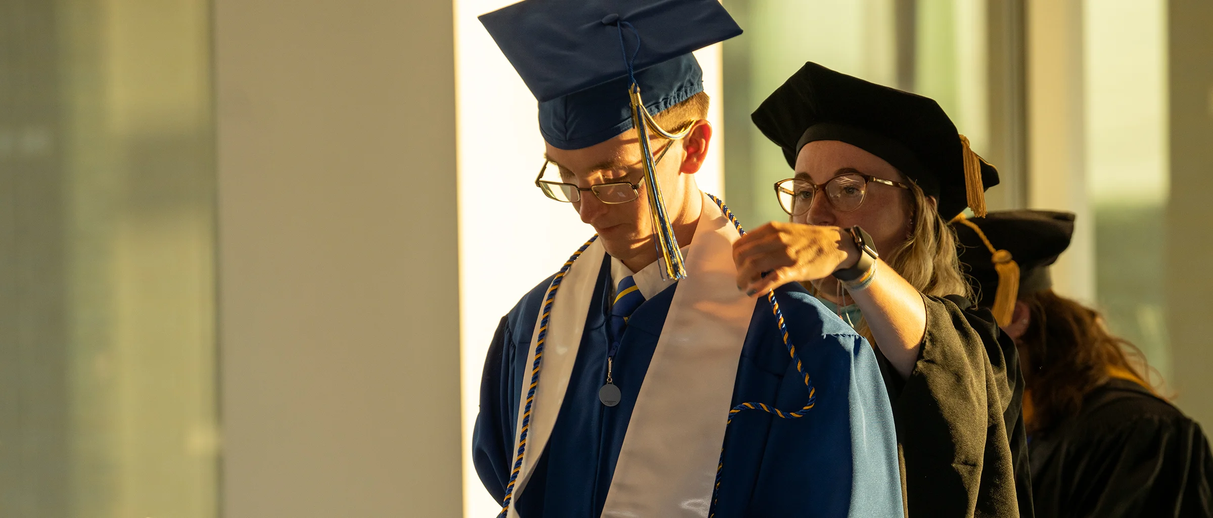 Jayla Godfrey places an honor cord over Zach Simpler's neck over his undergraduate academic regalia