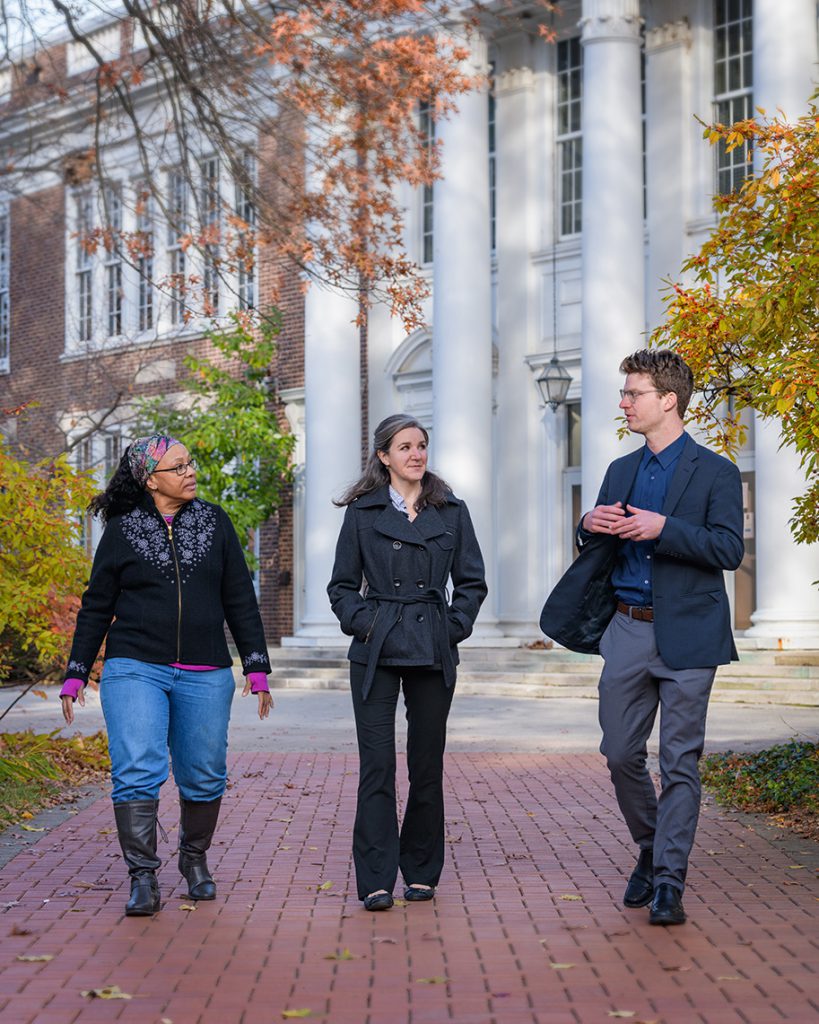 Three people walk along a brick path in the fall. Behind them is Pearson Hall, a neo-Georgian brick building with white columns.