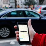 Potential Uber user holds smartphone on sidewalk