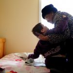 Group home staffer lifts a resident from her bed