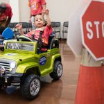 A young child with mobility impairment waves from his car during the Go Baby Go Memphis Rodeo