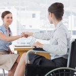 Female colleagues exchange a greeting, one is in a wheelchair