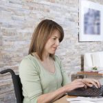 disabled woman types on laptop computer at dining room table