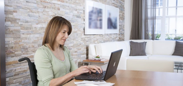 disabled woman types on laptop computer at dining room table