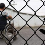 Man in a wheelchair seen through a fence