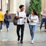 Two college students talk as they walk on a wide path with other pedestrians passing