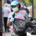 Brandy Oveal, with the Houston Independent School District Nutrition Services, prepares to help distribute bags of food while protecting herself from the virus