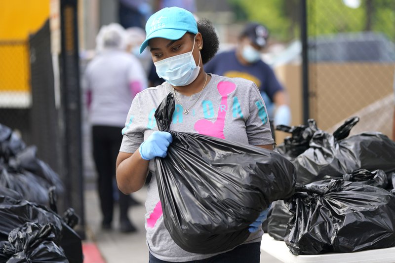 Brandy Oveal, with the Houston Independent School District Nutrition Services, prepares to help distribute bags of food while protecting herself from the virus
