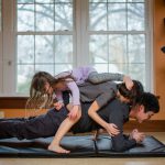 children playing on their father while he attempts to exercise in their home