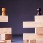 two chess pawns of opposing color standing apart on two separate stacks of wooden blocks