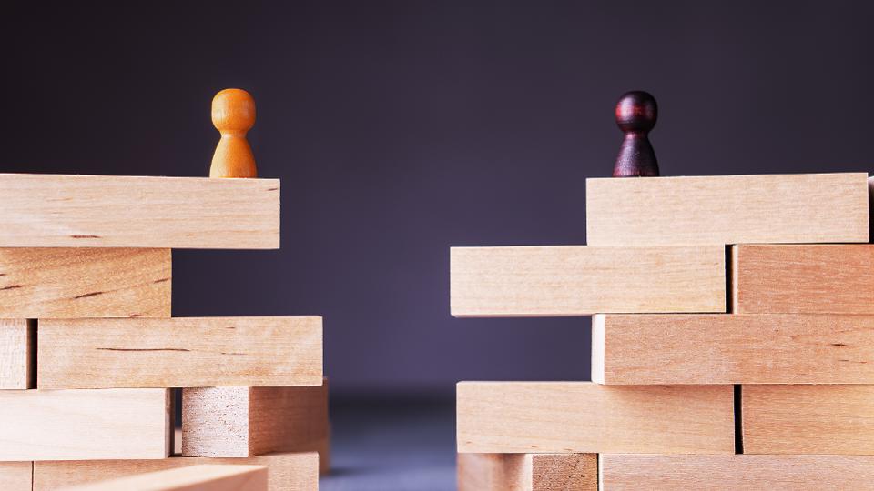 two chess pawns of opposing color standing apart on two separate stacks of wooden blocks