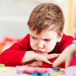 A child with autism sits frustrated at a table where others are doing school work