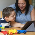 A child with a disability and his mother look at a tablet device together and smile
