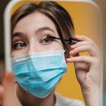 a woman wearing a face mask puts on eye makeup