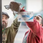 Job coach helps an employee who has a developmental disability with a troublesome spot on the outside glass door while working at a fitness center.