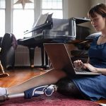 female college student with prosthetic leg sits on floor and works on a laptop