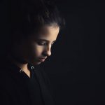 A teenage girl surrounded in black looks down sullenly