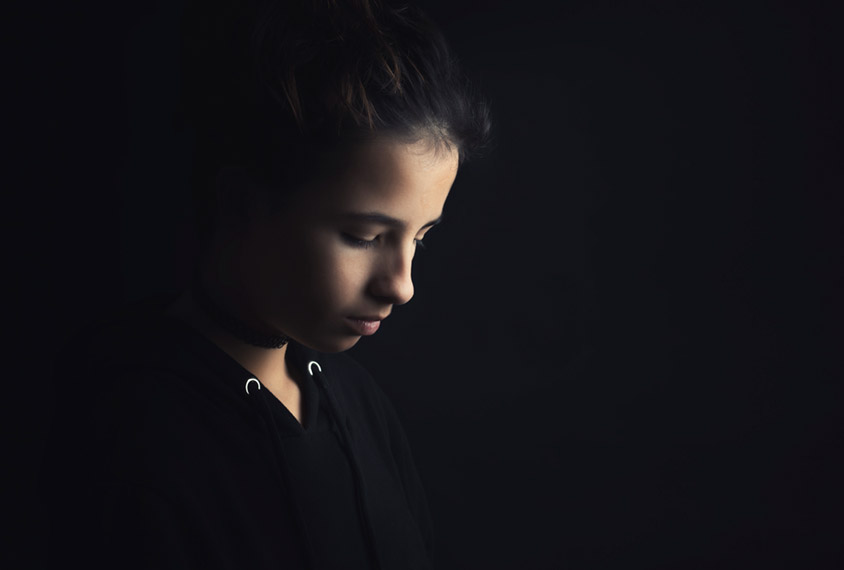 A teenage girl surrounded in black looks down sullenly