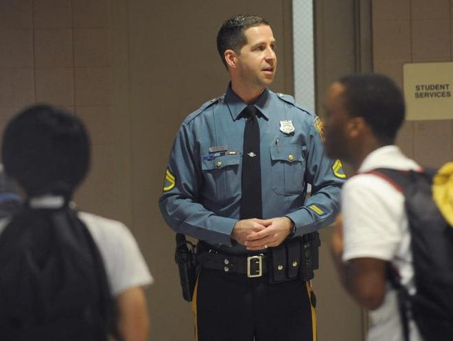 A police officer serving as a school resource officer stands in a school hallway.