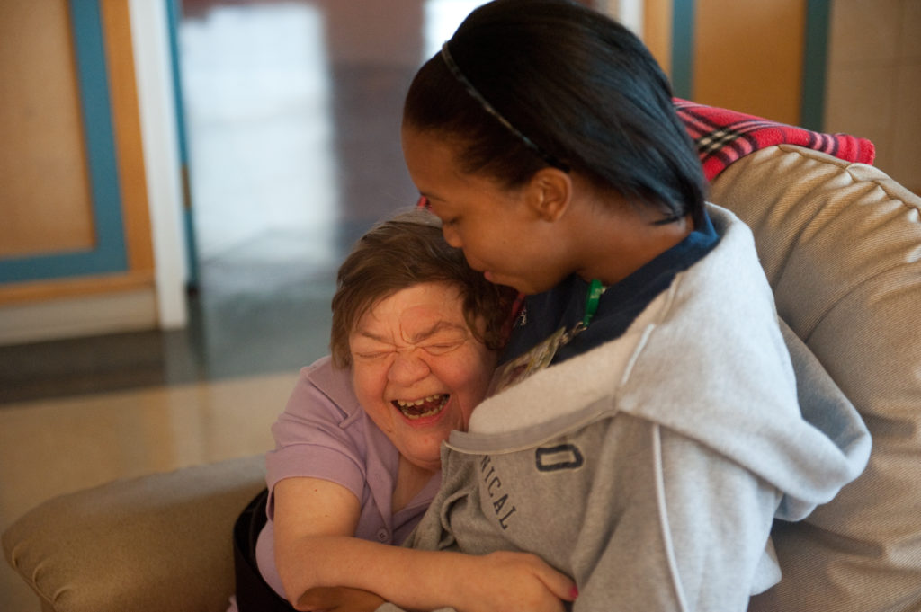 A resident and worker embrace at a intermediate care facility