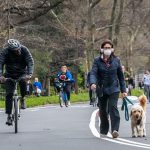An unmasked cyclist passes a masked pedestrian walking her dog