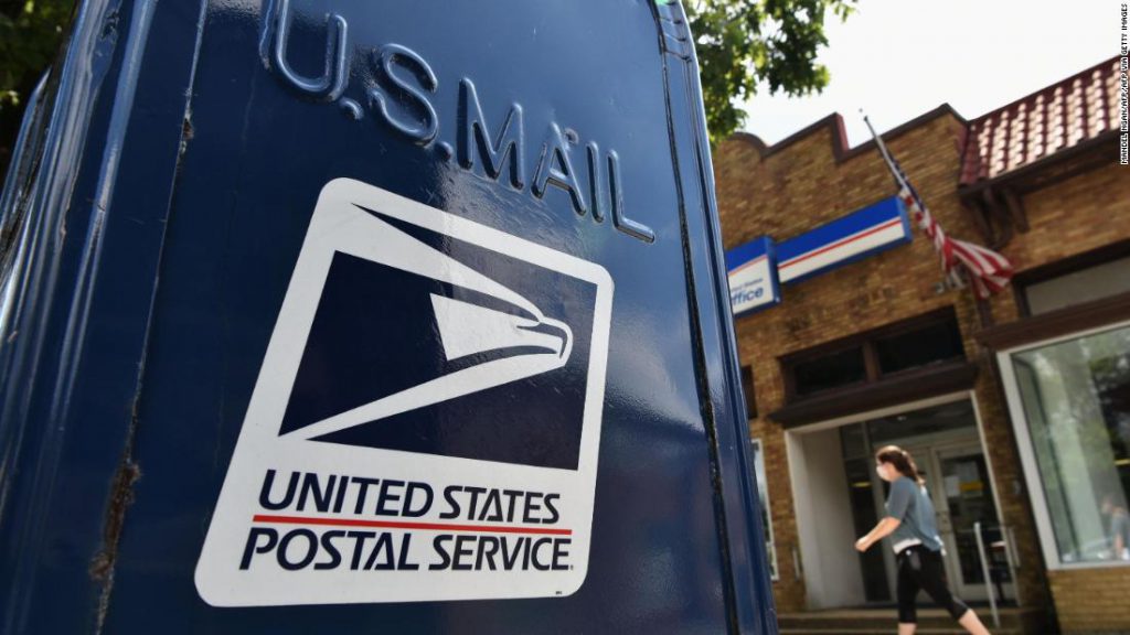 A United States Postal Service mailbox with a post office building in the background