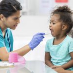 A school nurse dressed in scrubs takes a young girl's temperature.