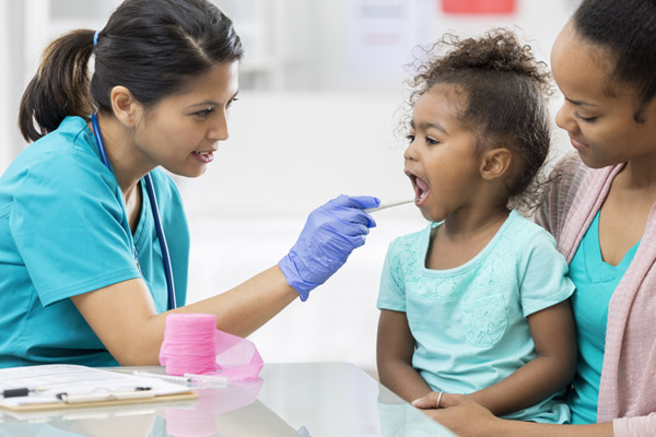 A school nurse dressed in scrubs takes a young girl's temperature.