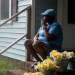 A woman sits smoking a cigarette on the stairs leading up to her residence