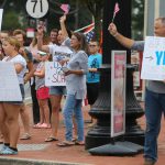 A small crowd stands on a sidewalk in Middletown, Delaware holding protest signs urging schools to open