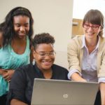 A young man uses a laptop while his mother and job coach watch, smiling