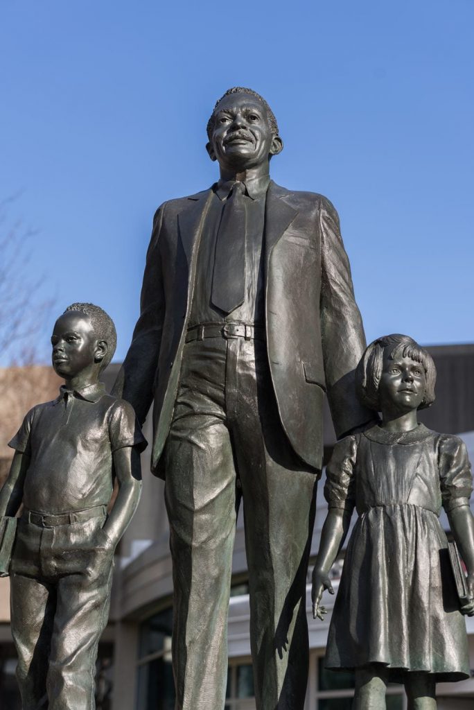 A statue of two children flanking Louis Redding, educational equity advocate, in a suit. Redding rests a hand on each child's shoulder