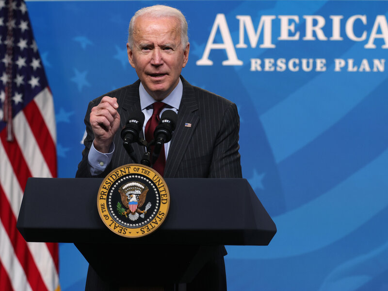 President Joe Biden speaks at a podium while behind him words read American Rescue Plan
