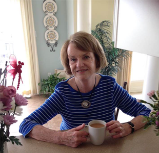 Alecia LaScala is an older woman with a brownish bob. She leans on a counter, holding a mug.