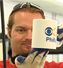 A young man with a VanDyke beard and sunglasses holds up a mug he has just impressed.