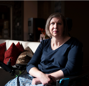 Julie Jennings sits in a powered wheelchair. Strong lighting falls on her from the left. Her right side is in shadow.