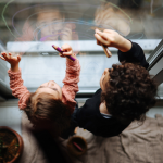 Two young children as seen from above, draw on a glass door.