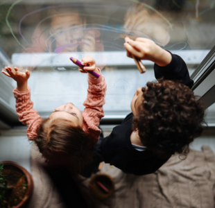 Two young children as seen from above, draw on a glass door.