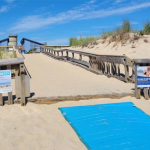 A dune crossing at the Delaware Seashore State Park. Just visible below sand are the wooden boards that make up the ramp. Worn wooden handrails line the ramp.