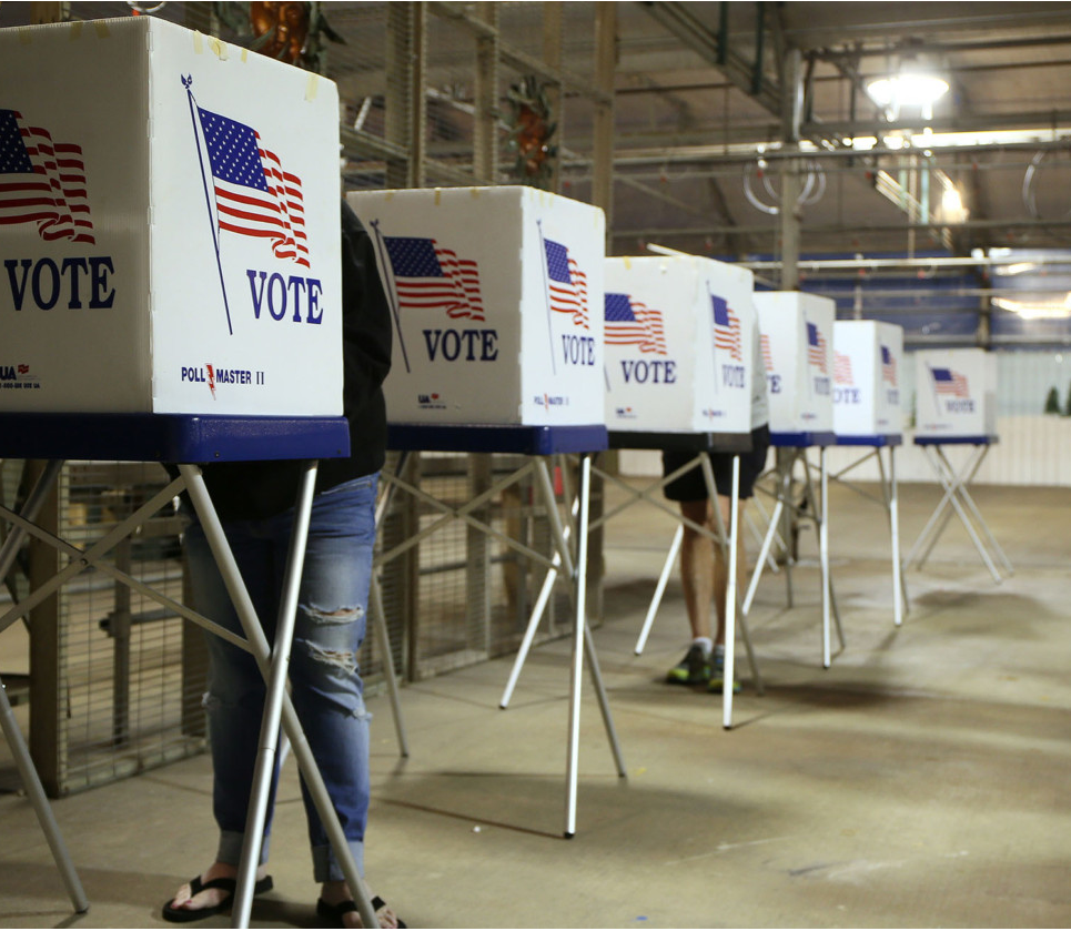 A line of temporary tables with voting blinds in a warehouse.