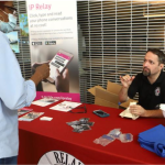Feta Fernsler from Delaware Relay sits behind a table and engages with a visitor