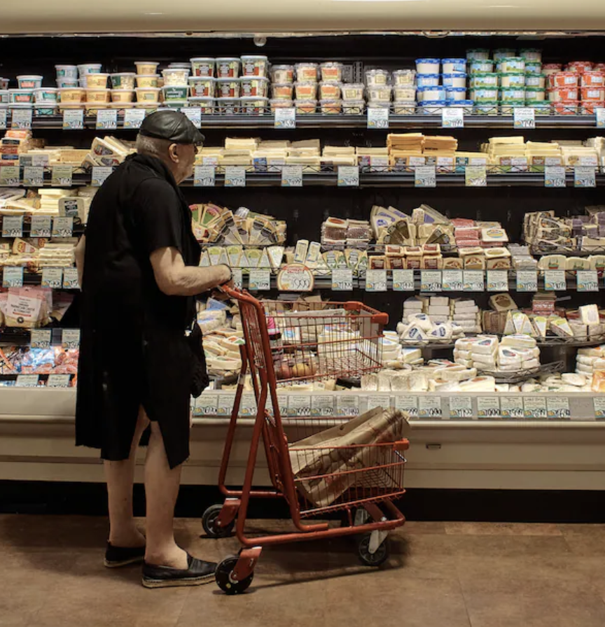 An older shopper browses in the cheese case at a New York supermarket.
