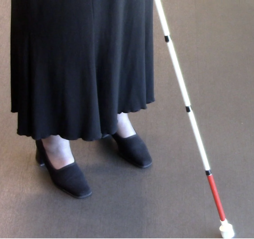 Feet of a person in a skirt using a white cane.