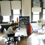 A teacher at Nebinger Elementary School in Philadelphia in 2021. The classroom has a big bank of window, a window unit air conditioner and shiny wooden floors.