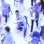 A student sits in a classroom desk, leaning their head on their hand and an unengaged expression as students in motion move around them.