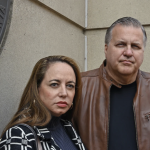 Vivian and Trevor Chaplick stand in front of a concrete building.
