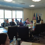 Chuck Sawchenko leads a training session for first responders. Attendees are seated around a conference table and around the room. Many wear various uniforms.