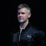 John McFall is a light skinned man with short grey hair, wearing a black satin European Space Agency jacket.