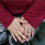 Hands in a lap. The hands have longer fingernails, some wrinkles and a wedding set.