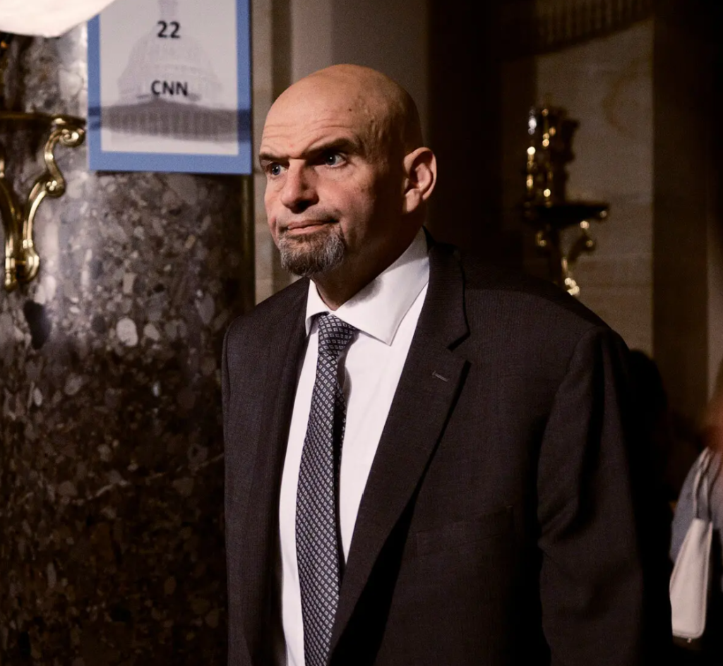 US Senator John Fetterman is a tall man with a bald head, strong eyebrows and a beard. He wears a suit and tie.